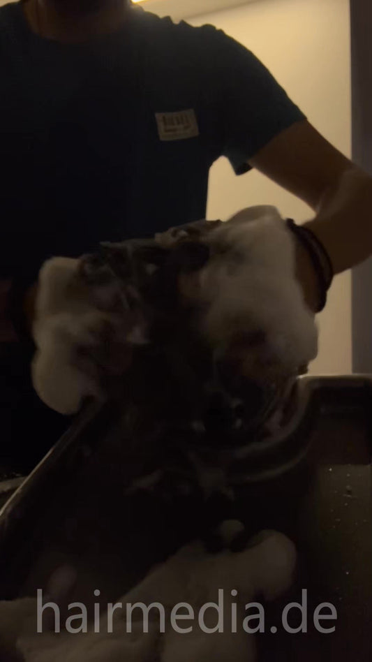 2032 Nikos Barber 250527 Barber Nikos is shampooing Giannis in the kitchen in a dark room.