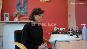 1180 MichelleB by barber 1 waiting a lone in barberchair in Berlin salon in black large vinyl cape